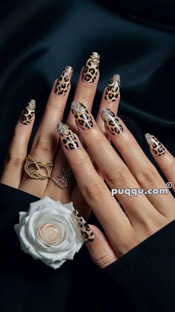 Hands with long leopard print nails adorned with gold and silver glitter, wearing gold rings and holding a white rose.