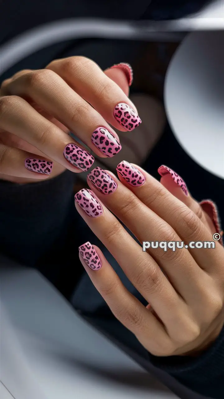 Hands with long nails decorated in a pink and black leopard print pattern.