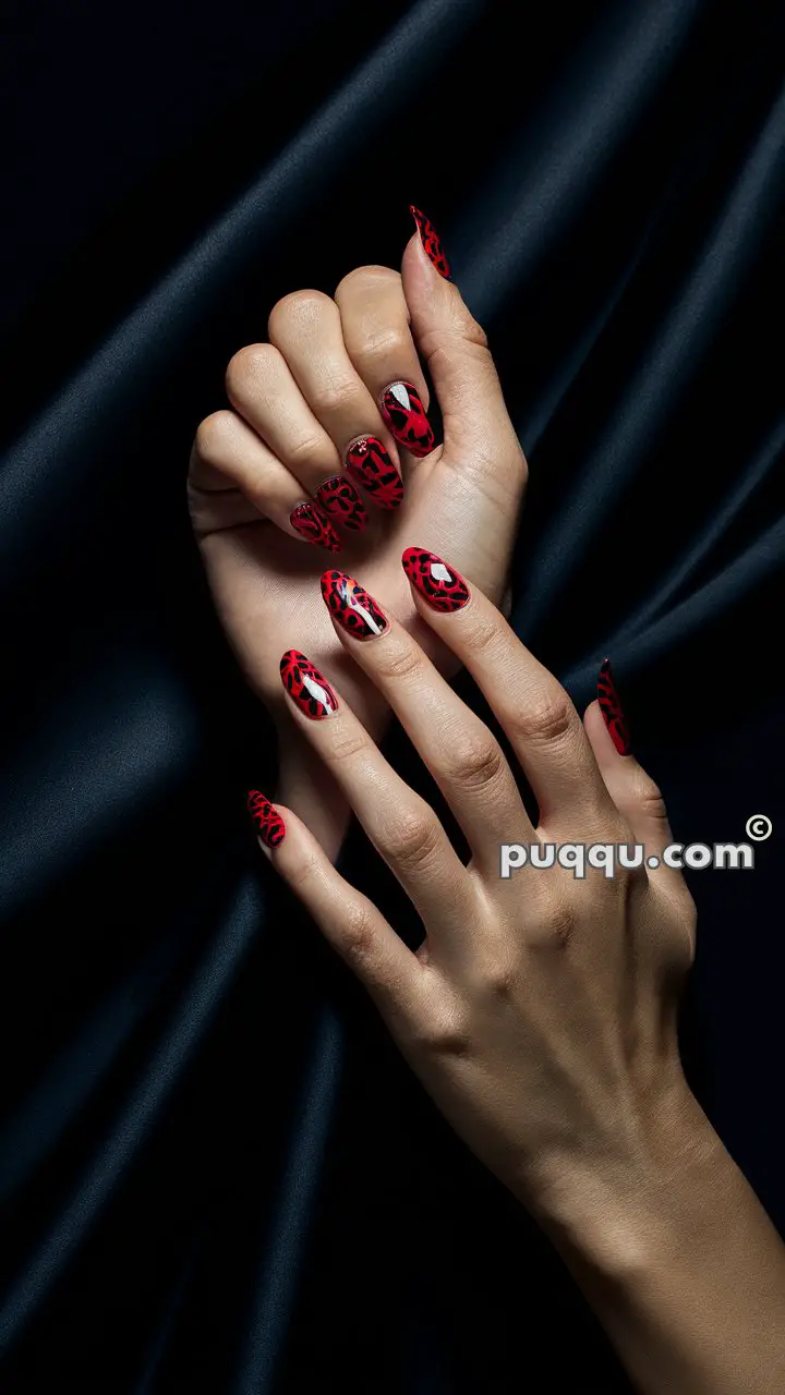 Hands with long red nails featuring a black leopard print design, set against a dark background.