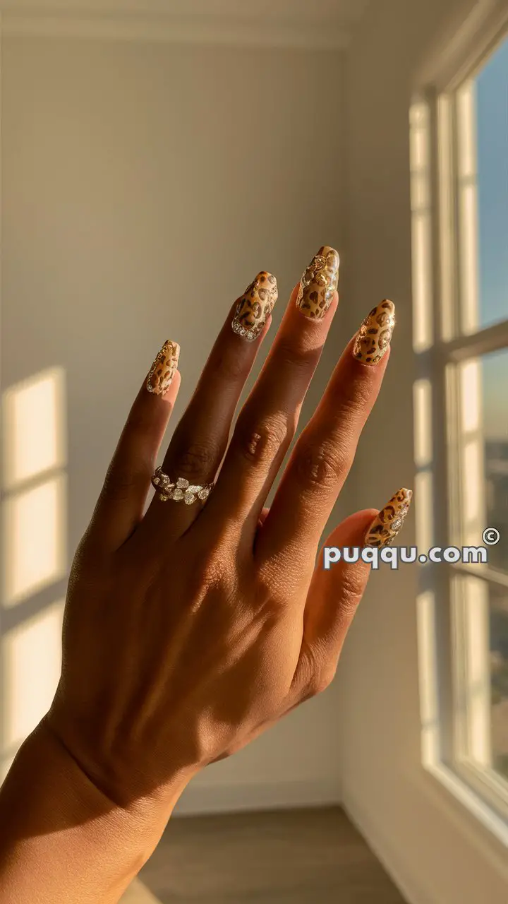 Hand with gold and leopard print nails, wearing a silver ring with floral designs, in front of a window with natural light.