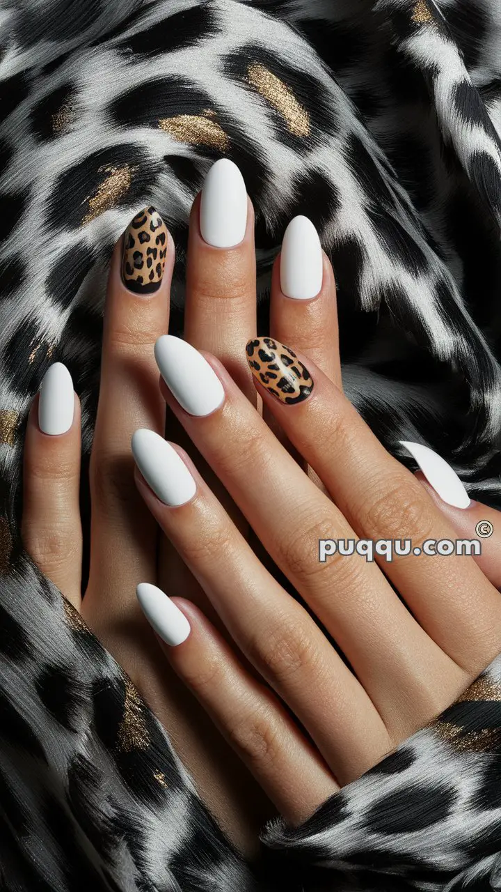 Hands with long, almond-shaped nails painted white, with one accent nail featuring a leopard print design, against a leopard print fabric background.