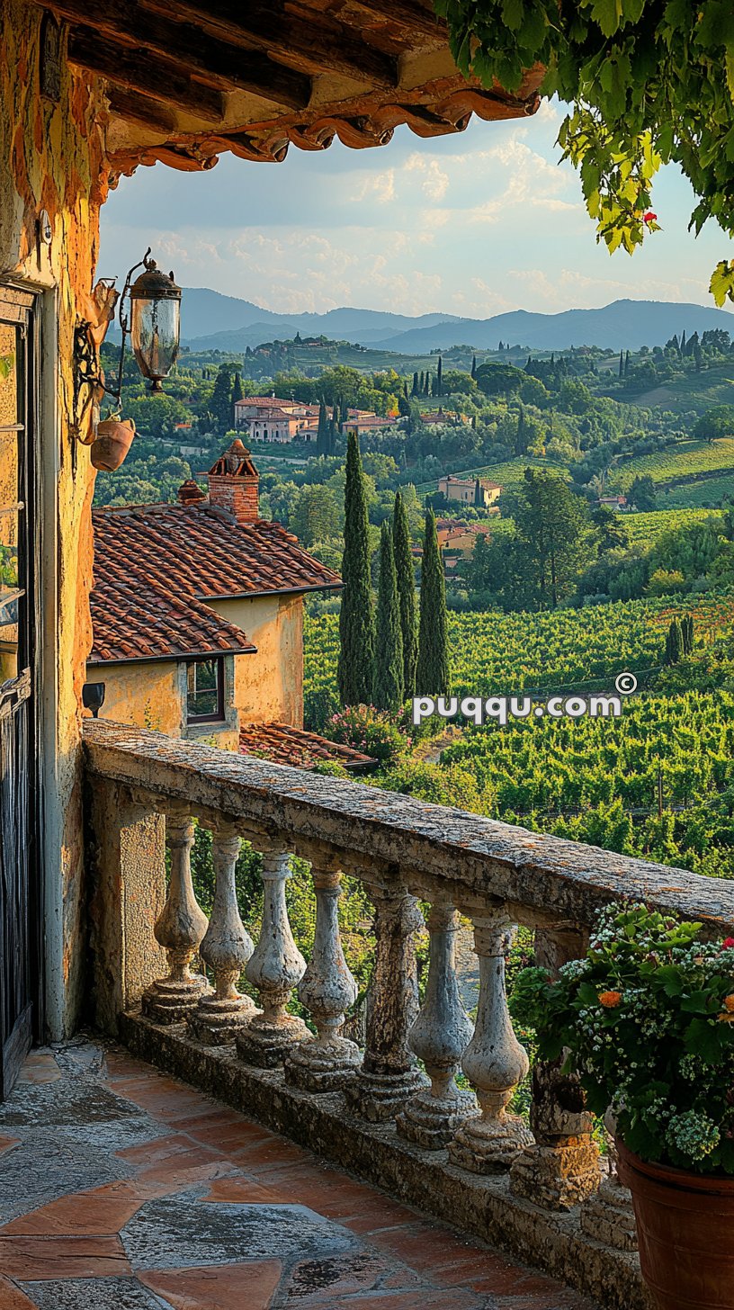 View from a rustic balcony overlooking a vineyard and rolling hills with cypress trees and traditional Italian buildings in the distance.