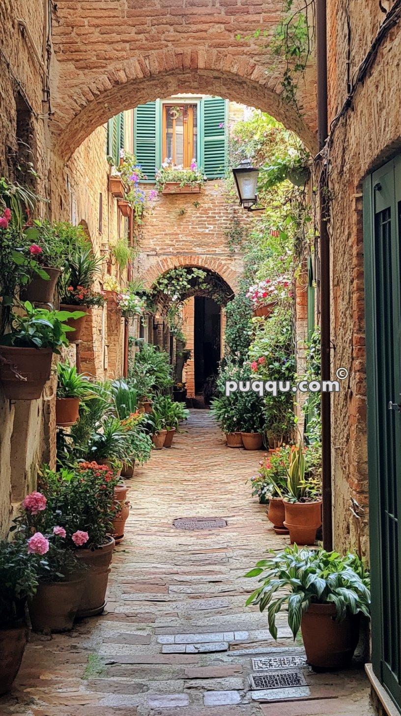 A narrow cobblestone alley lined with potted plants and flowers, featuring an arched passageway and windows with green shutters.