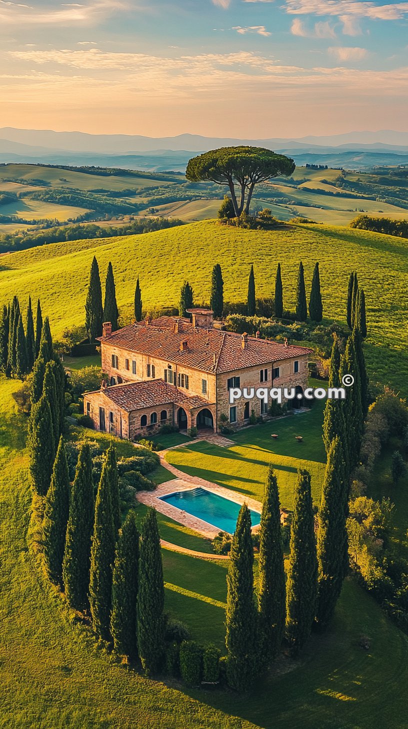 Aerial view of a large villa with terracotta roof, surrounded by cypress trees, a swimming pool, and a verdant landscape of rolling hills.