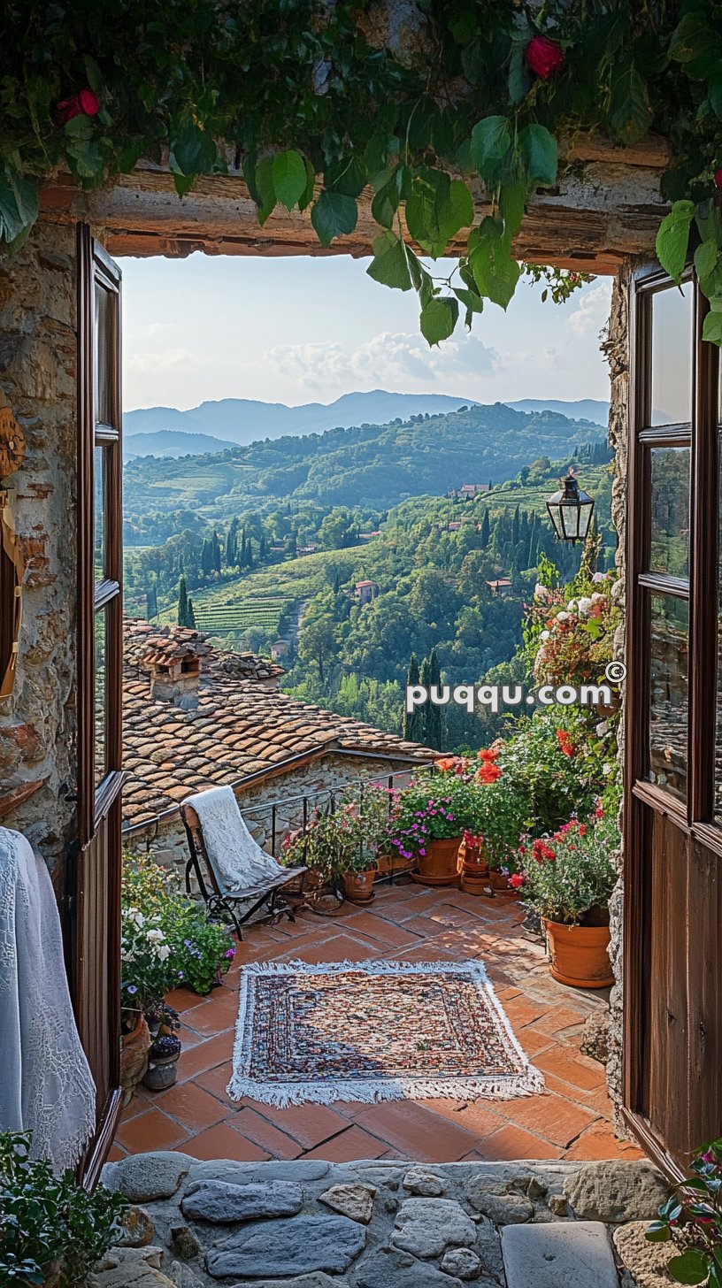 Open doorway leads to a picturesque terrace with a rug and potted plants, overlooking a scenic landscape of rolling green hills and distant mountains under a partly cloudy sky.