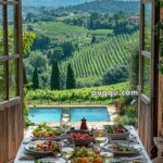 A rustic table set with salads, fruits, and wine overlooks a vineyard and mountains through open wooden doors, with a pool in the foreground.