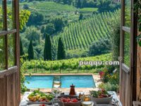 A rustic table set with salads, fruits, and wine overlooks a vineyard and mountains through open wooden doors, with a pool in the foreground.