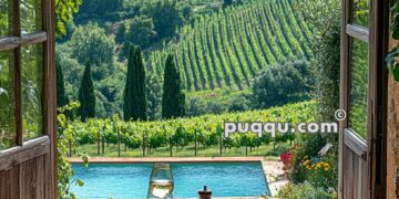 A rustic table set with salads, fruits, and wine overlooks a vineyard and mountains through open wooden doors, with a pool in the foreground.