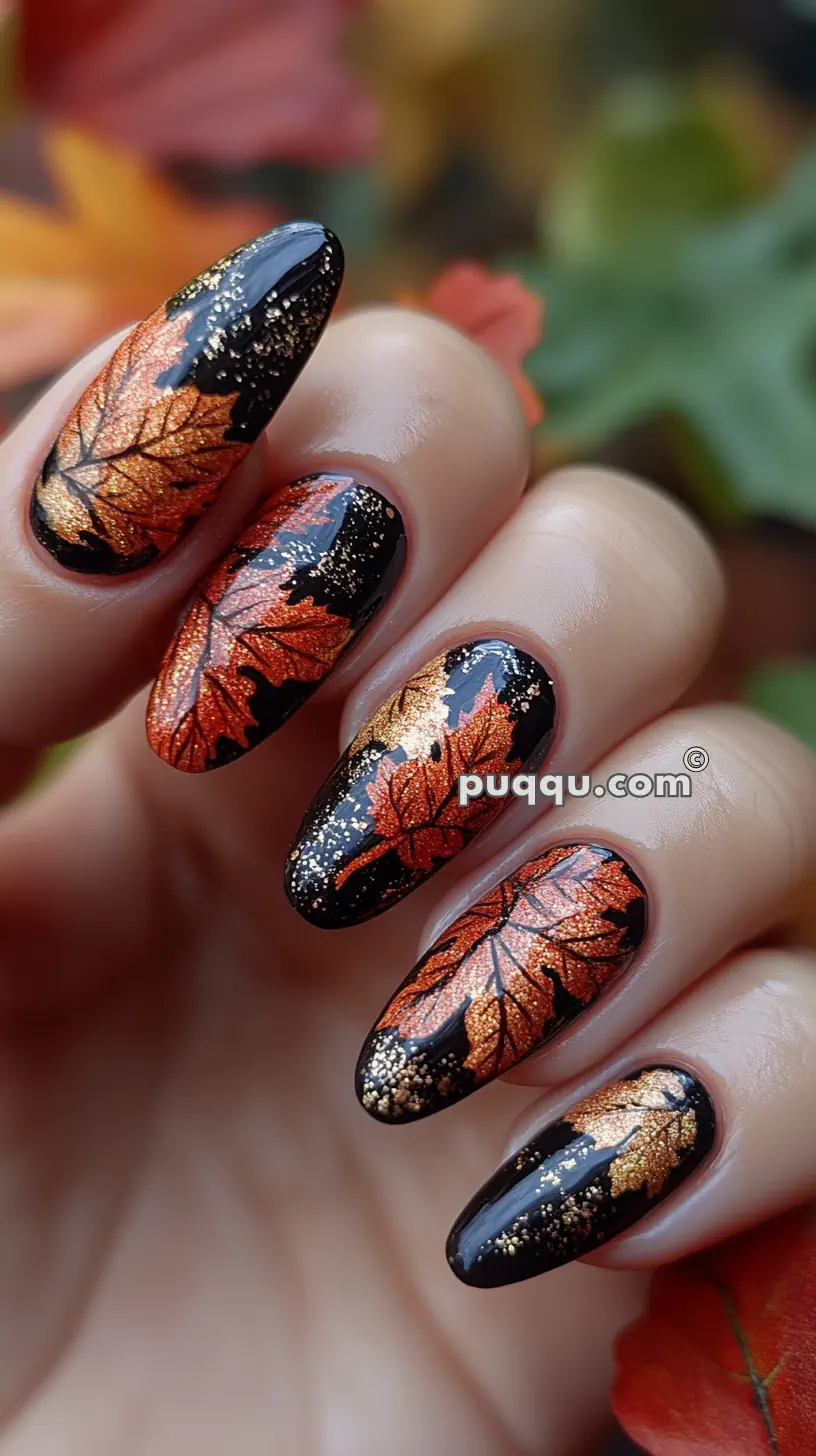 Close-up of a hand with long nails painted black with orange and gold autumn leaves and glitter accents.