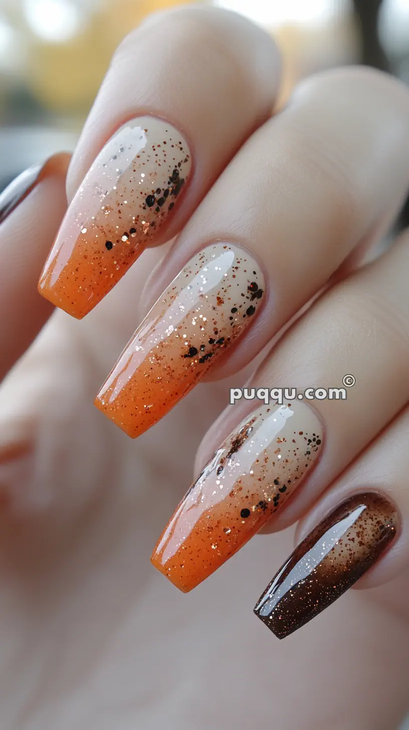 Long nails with an orange ombre gradient, black speckles, and glittery accents.