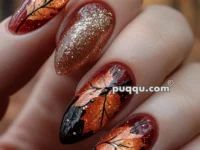 Nails with an autumn-themed design featuring intricate orange leaf patterns and gold glitter accents.