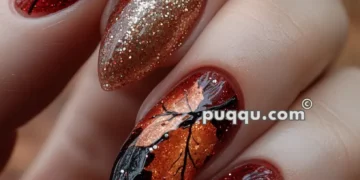 Nails with an autumn-themed design featuring intricate orange leaf patterns and gold glitter accents.