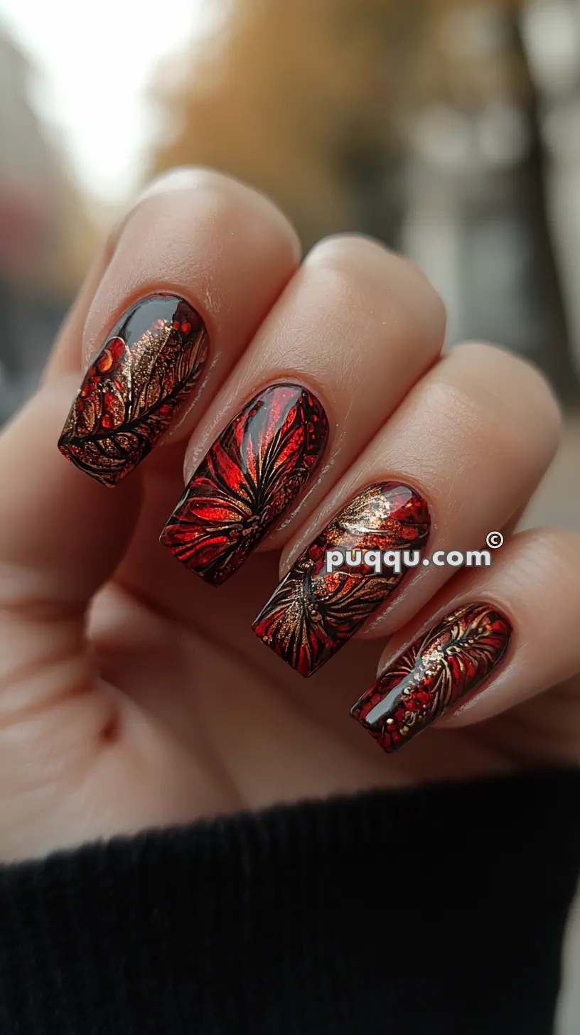 A hand with red and black butterfly-themed nail art with golden accents on long, square-shaped nails.