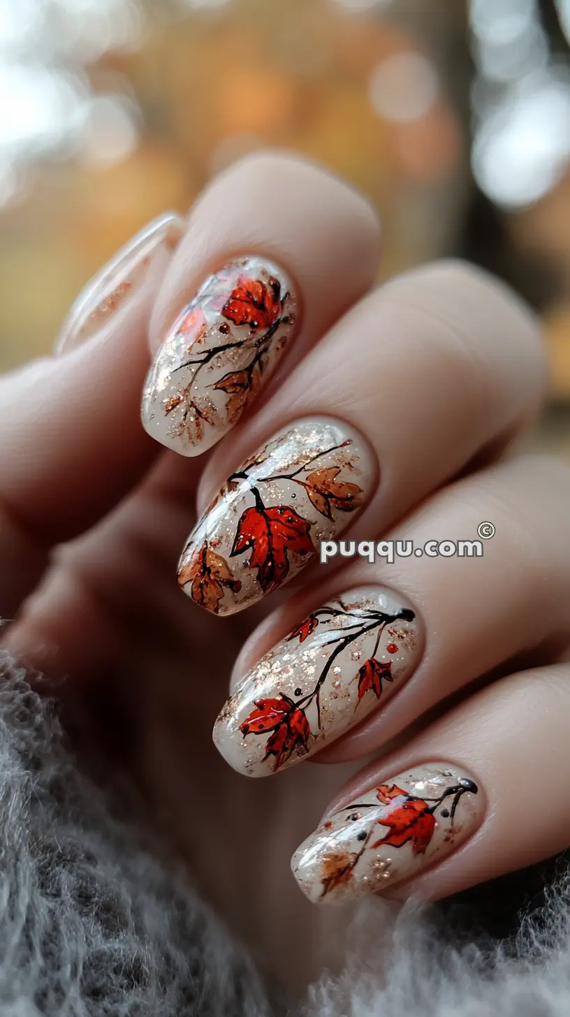 Close-up of nails with an autumn-themed design featuring red and brown leaves on a glittery beige background.