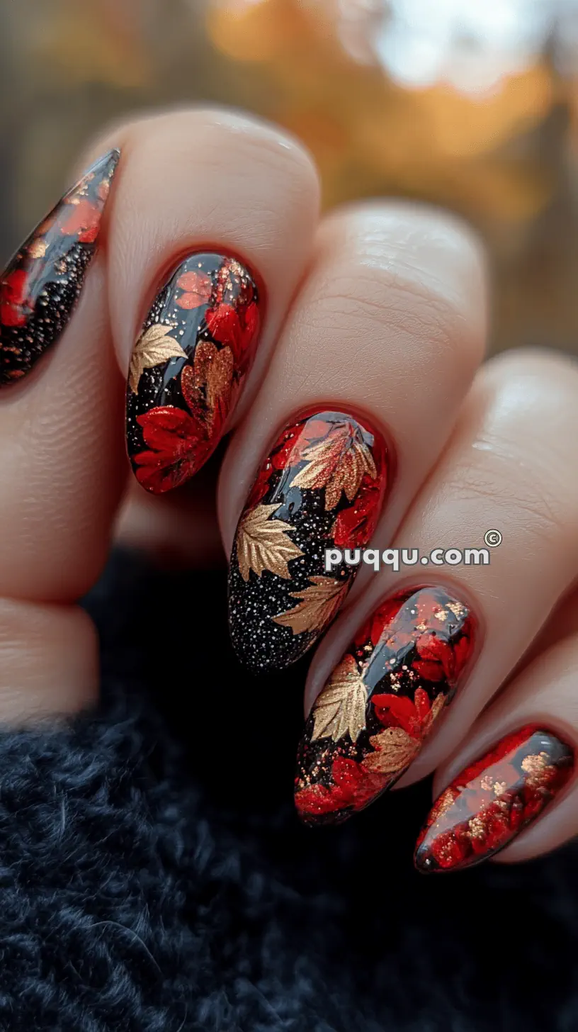 Close-up of a hand with long, almond-shaped nails featuring a black base with red and gold autumn leaf designs.