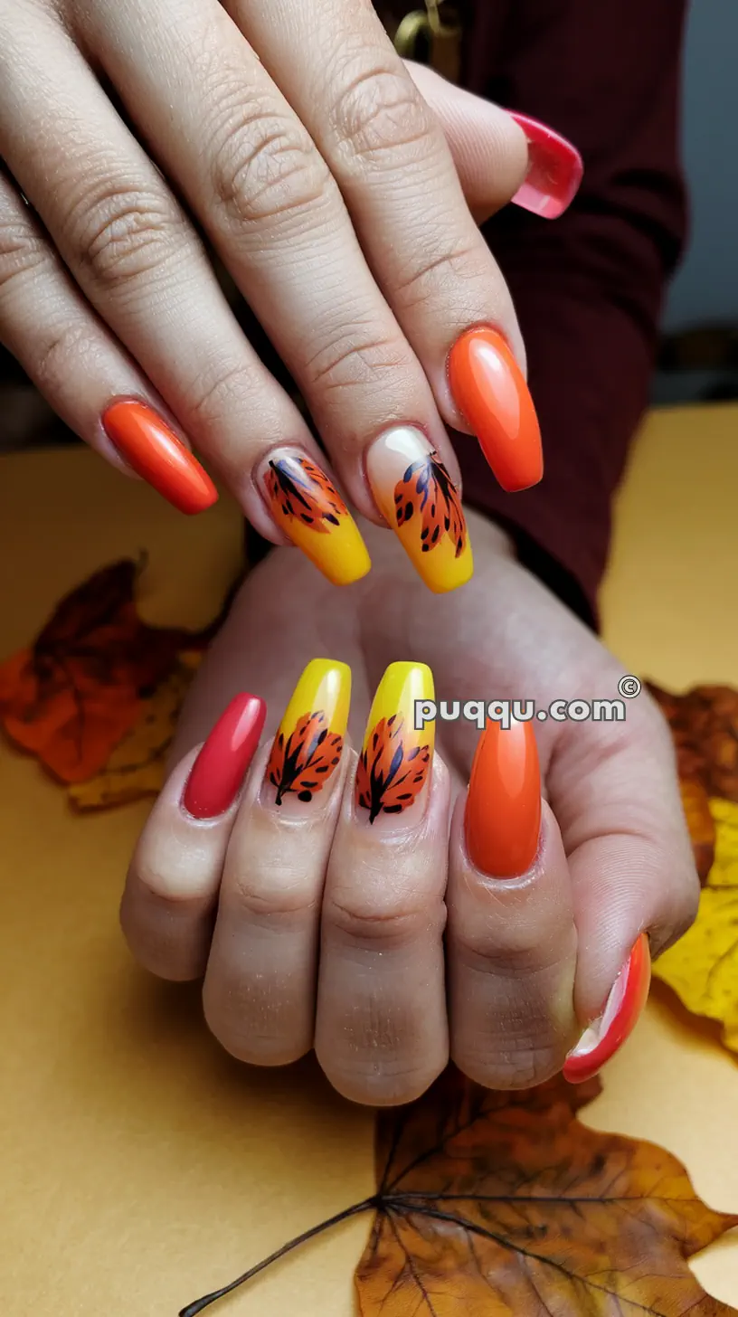 Hands with long, oval-shaped nails painted in autumn-themed colors of orange, red, and yellow with black leaf designs.