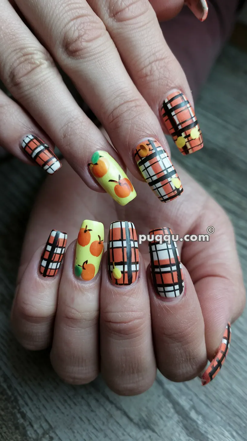 Hands with long, square nails painted with a mix of orange and black plaid patterns and yellow polish with small orange fruits.