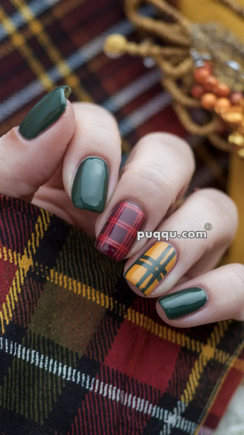 A close-up of a hand with a plaid patterned fabric in the background, displaying green nail polish on the thumb, index, and pinky fingers, and multicolored plaid designs on the middle and ring fingers.