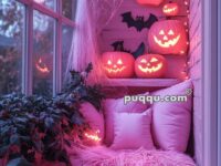 Cozy corner with pink pillows and fluffy blanket decorated for Halloween with glowing jack-o'-lanterns, fake spider webs, and bat cutouts.