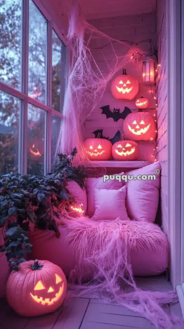 Cozy corner with pink pillows and fluffy blanket decorated for Halloween with glowing jack-o'-lanterns, fake spider webs, and bat cutouts.