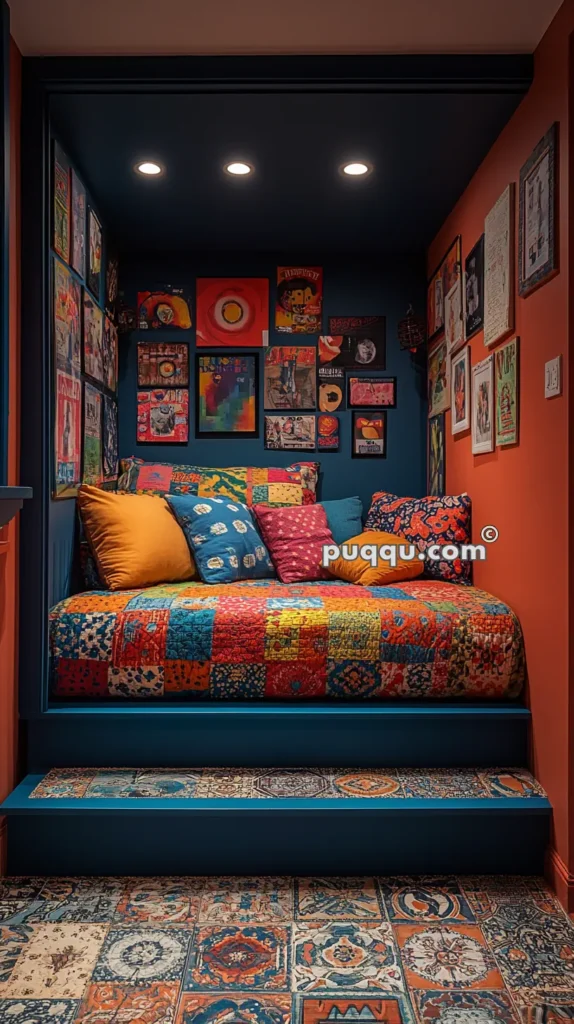 Cozy nook with colorful patchwork bedding, surrounded by eclectic framed artwork on dark blue walls, illuminated by recessed ceiling lights, with patterned tile flooring and steps leading up to the bed.