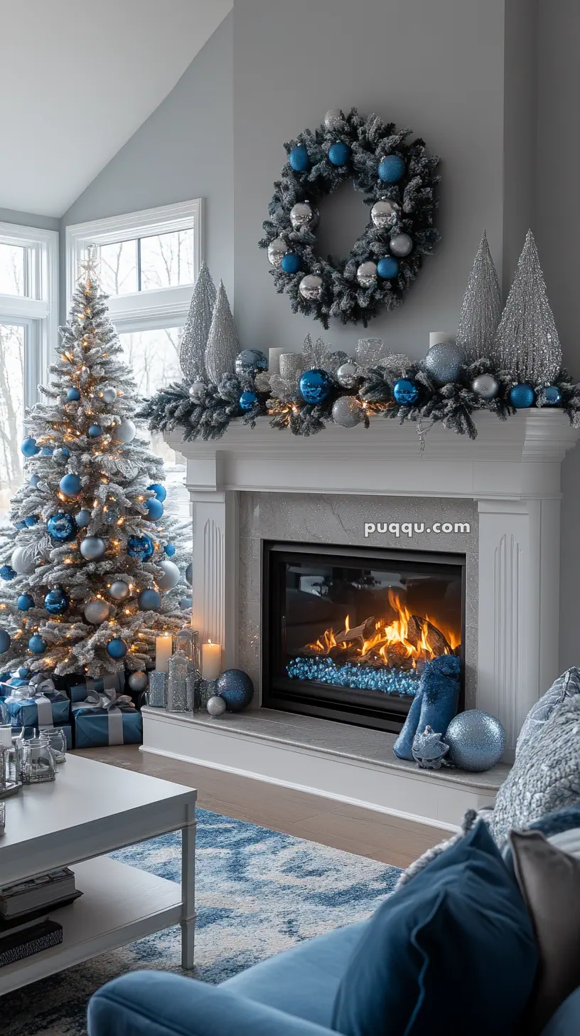 Cozy living room with a Christmas tree decorated in blue and silver, a lit fireplace, and a festive wreath above the mantel.