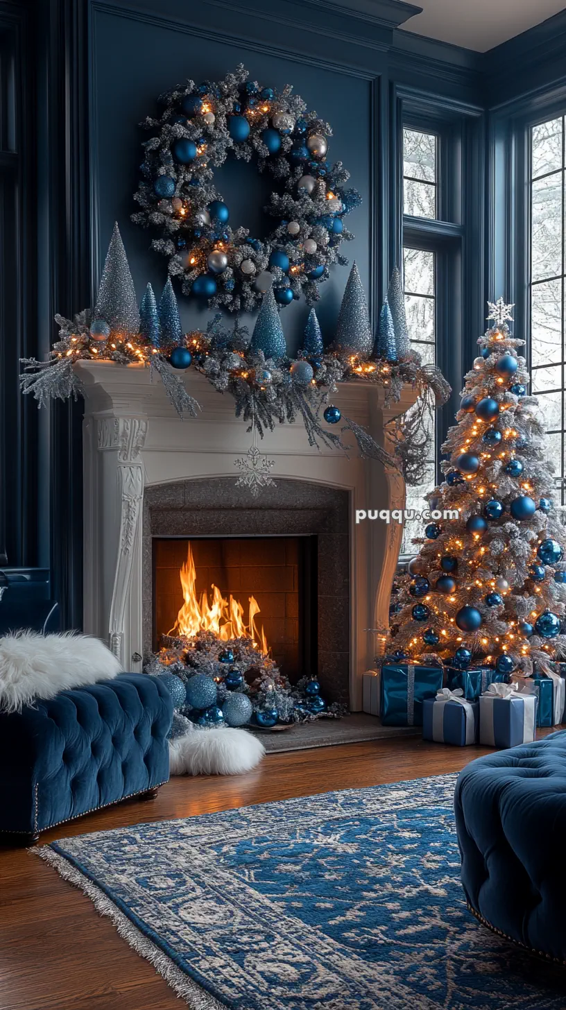 Elegant living room with a lit fireplace, decorated in blue and silver Christmas theme, featuring a wreath, Christmas tree, and wrapped gifts.