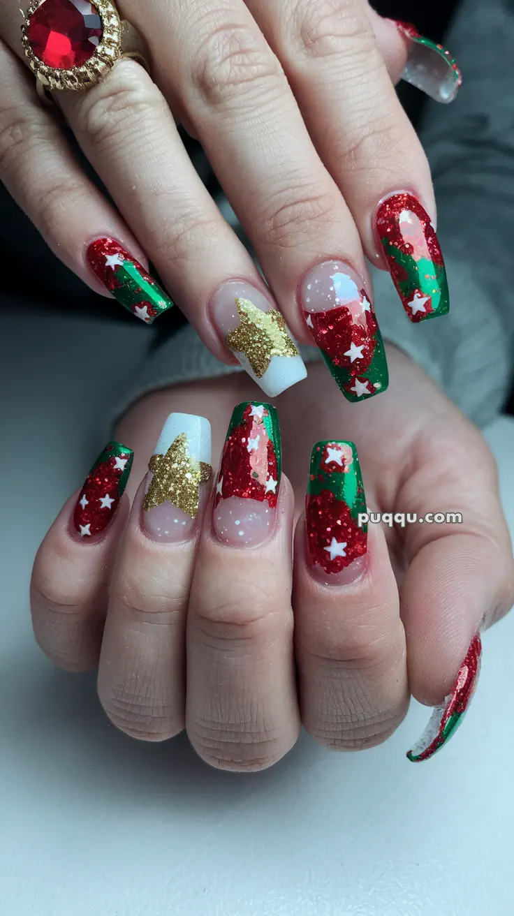 Fingernails with festive Christmas-themed nail art, featuring red, green, and white colors, gold glitter stars, and a red gemstone ring on one finger.