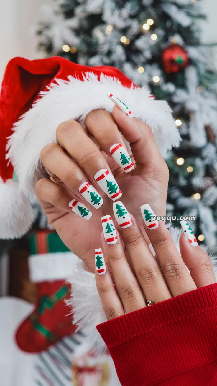 Festive nail art with Christmas tree and Santa hat designs, in front of a decorated Christmas tree.