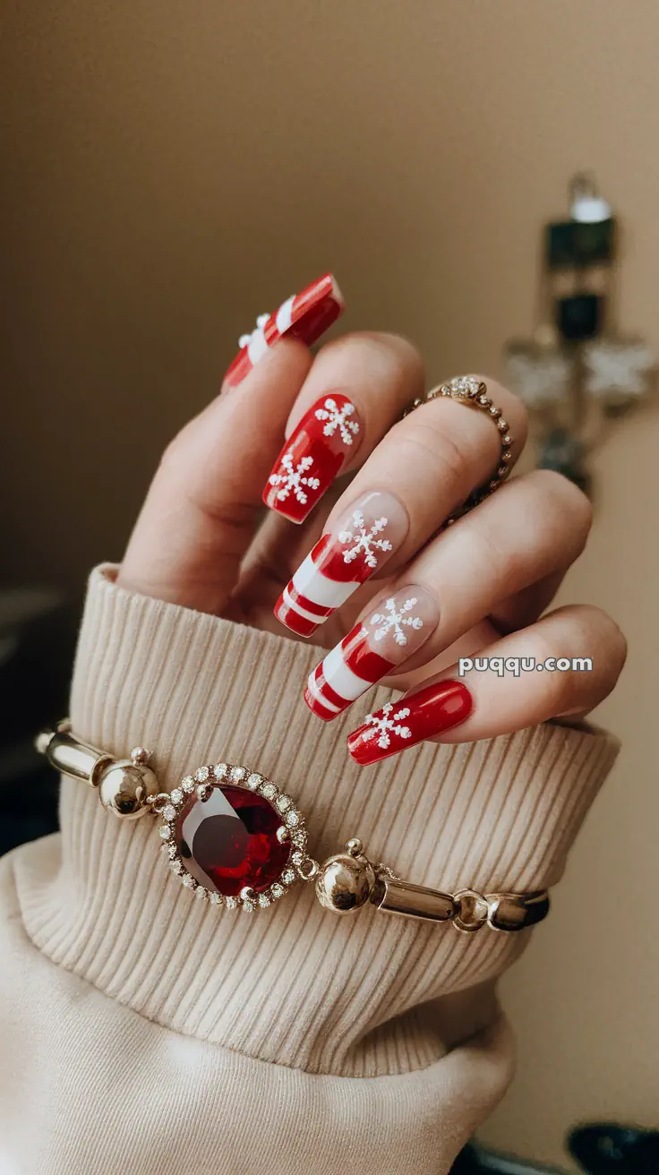 Hand with festive red and white striped nails featuring snowflake designs, wearing a gold bracelet with a large red stone.