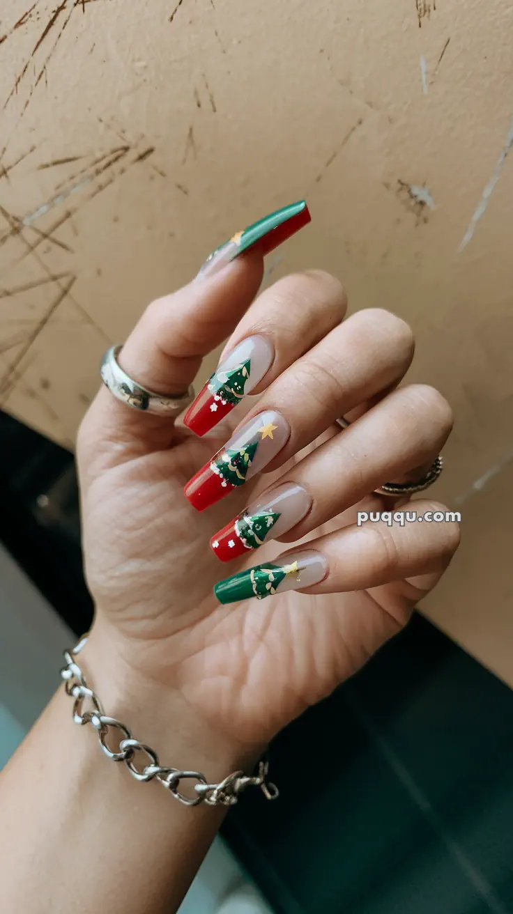 Hand with long nails decorated with festive Christmas tree designs in red and green.