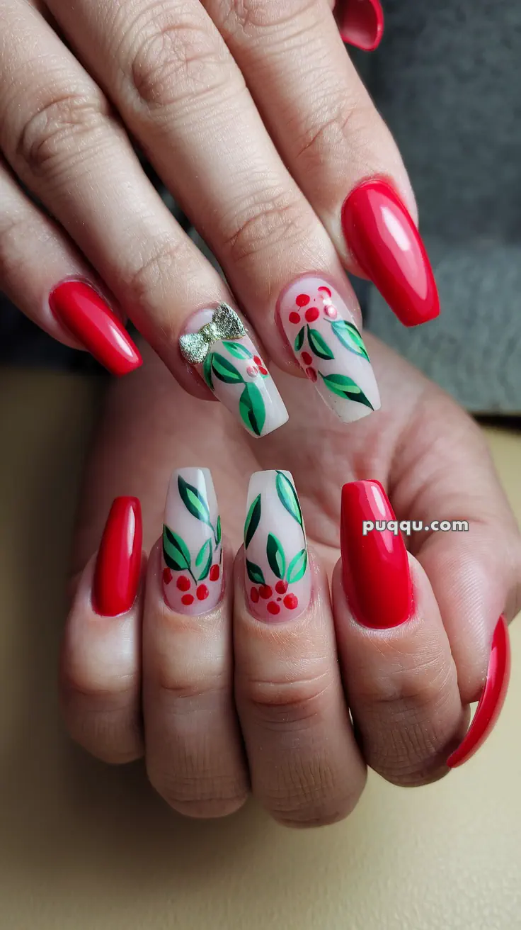 Nails with red polish and floral designs featuring green leaves and red dots on a few nails, with a small silver bow ornament.