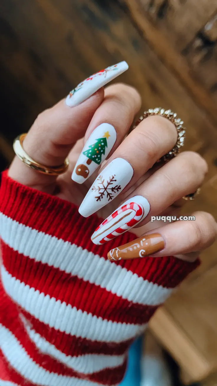 Hand with Christmas-themed nail art, including a Christmas tree, snowflakes, candy cane, and gingerbread design, wearing a red and white striped sweater.