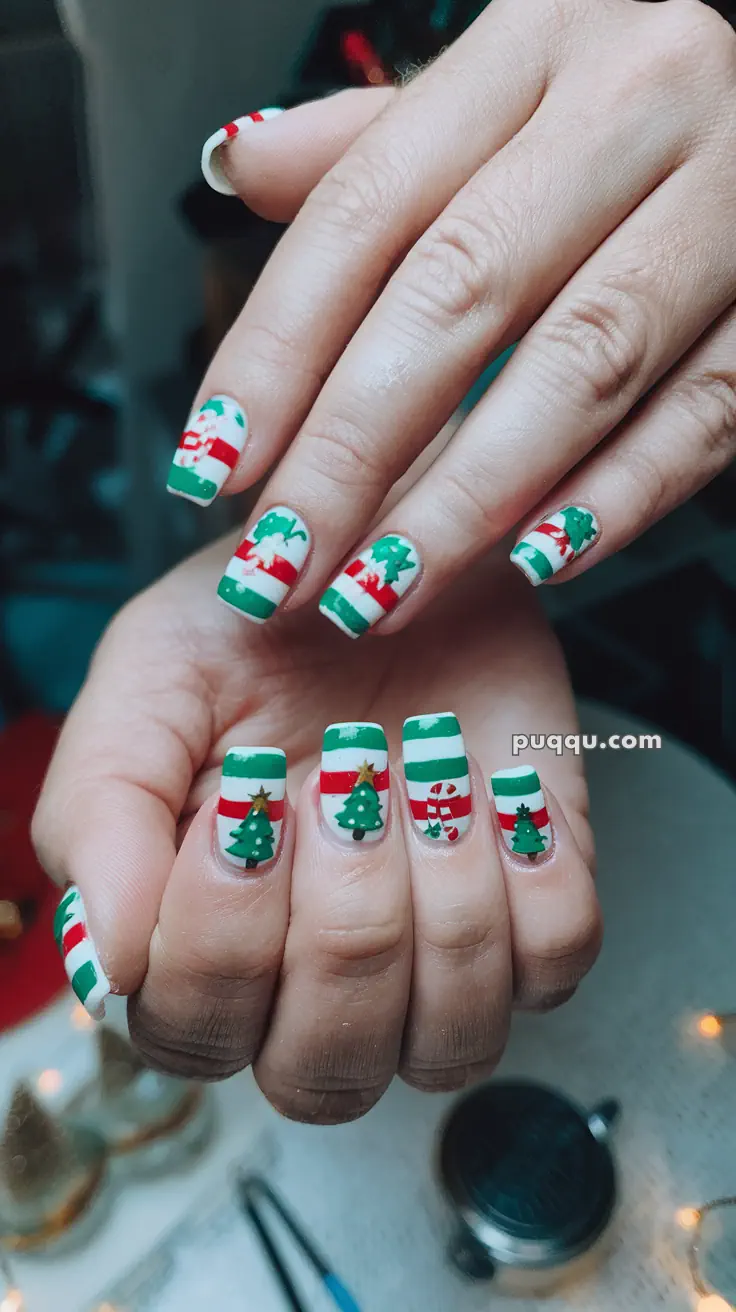 Close-up of Christmas-themed nail art with red, green, and white stripes, featuring designs of Christmas trees, snowflakes, and candy canes.