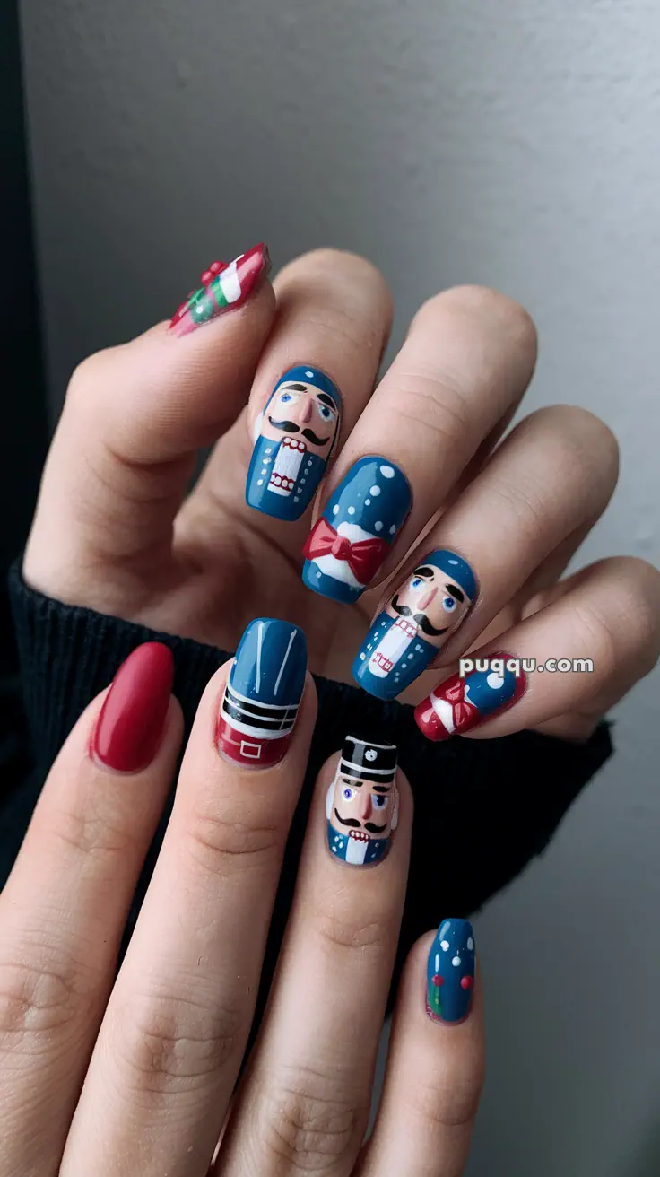 Fingernails with festive nutcracker designs in blue, red, and white, featuring detailed faces and patterns.