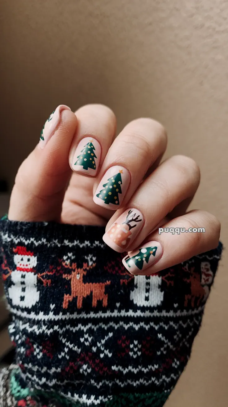 Nails with Christmas tree and reindeer designs, held by a person wearing a festive sweater.