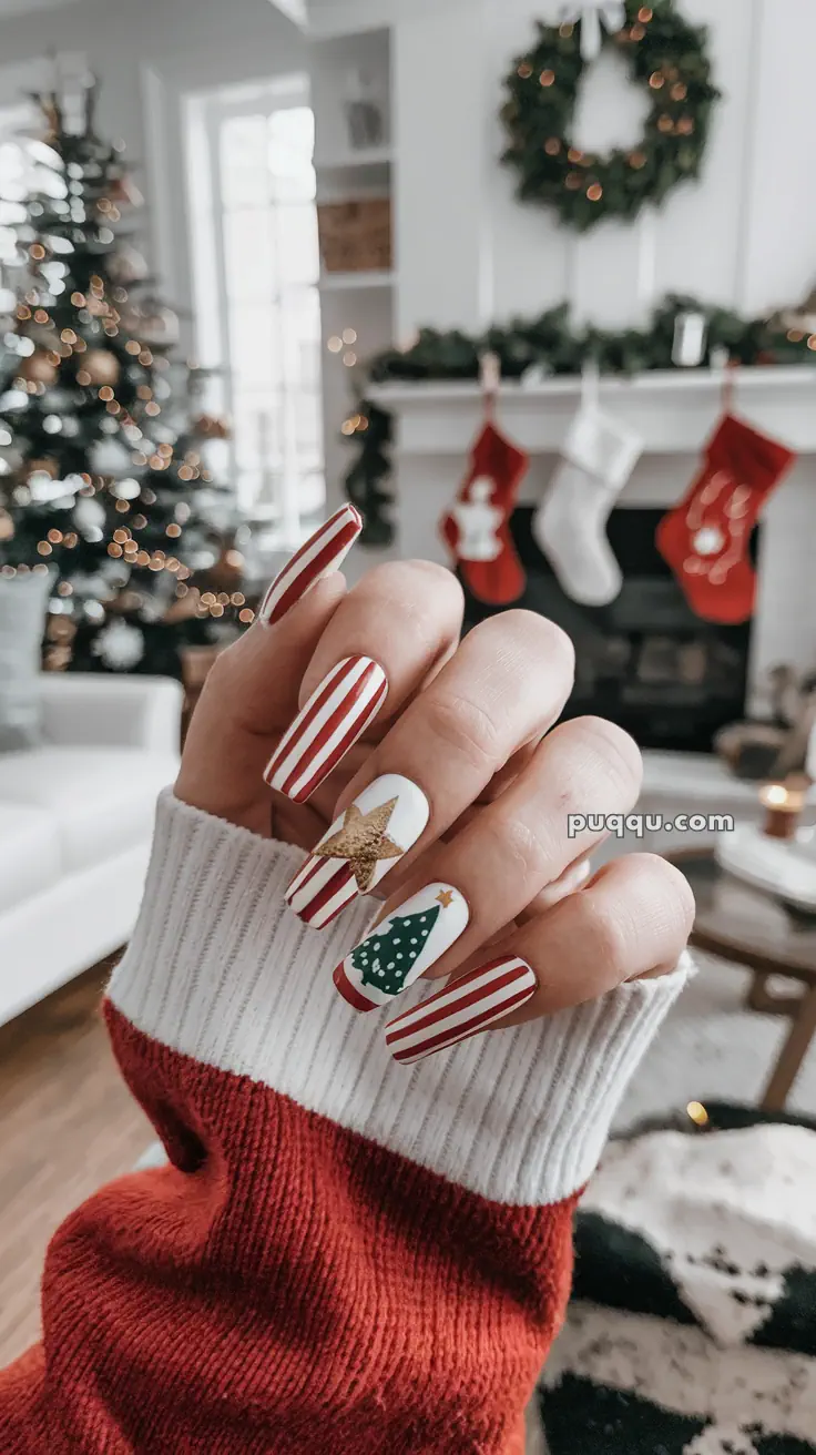 A hand with festive red and white striped nails and Christmas-themed designs, in a holiday-decorated living room with a Christmas tree, stockings, and wreath.