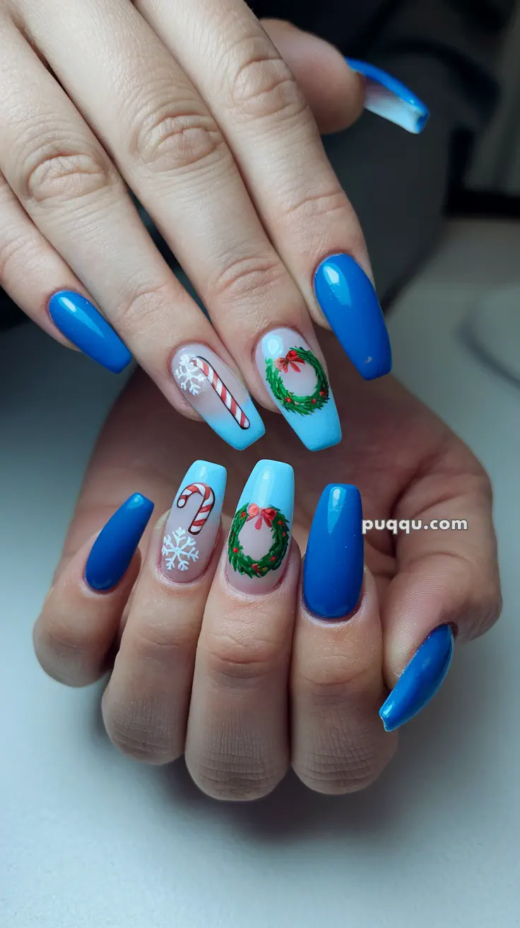 Blue and light blue acrylic nails with holiday-themed designs, including candy canes, wreaths, and snowflakes.