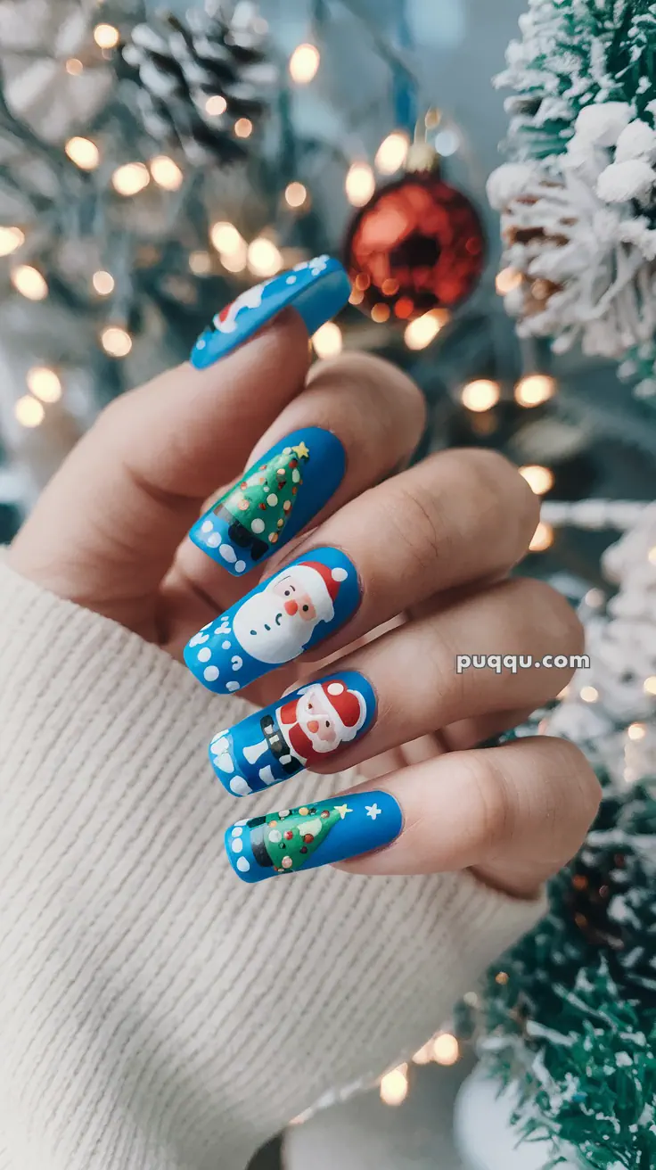 Festive Christmas-themed nail art with Santa Claus and Christmas tree designs against a blue background.