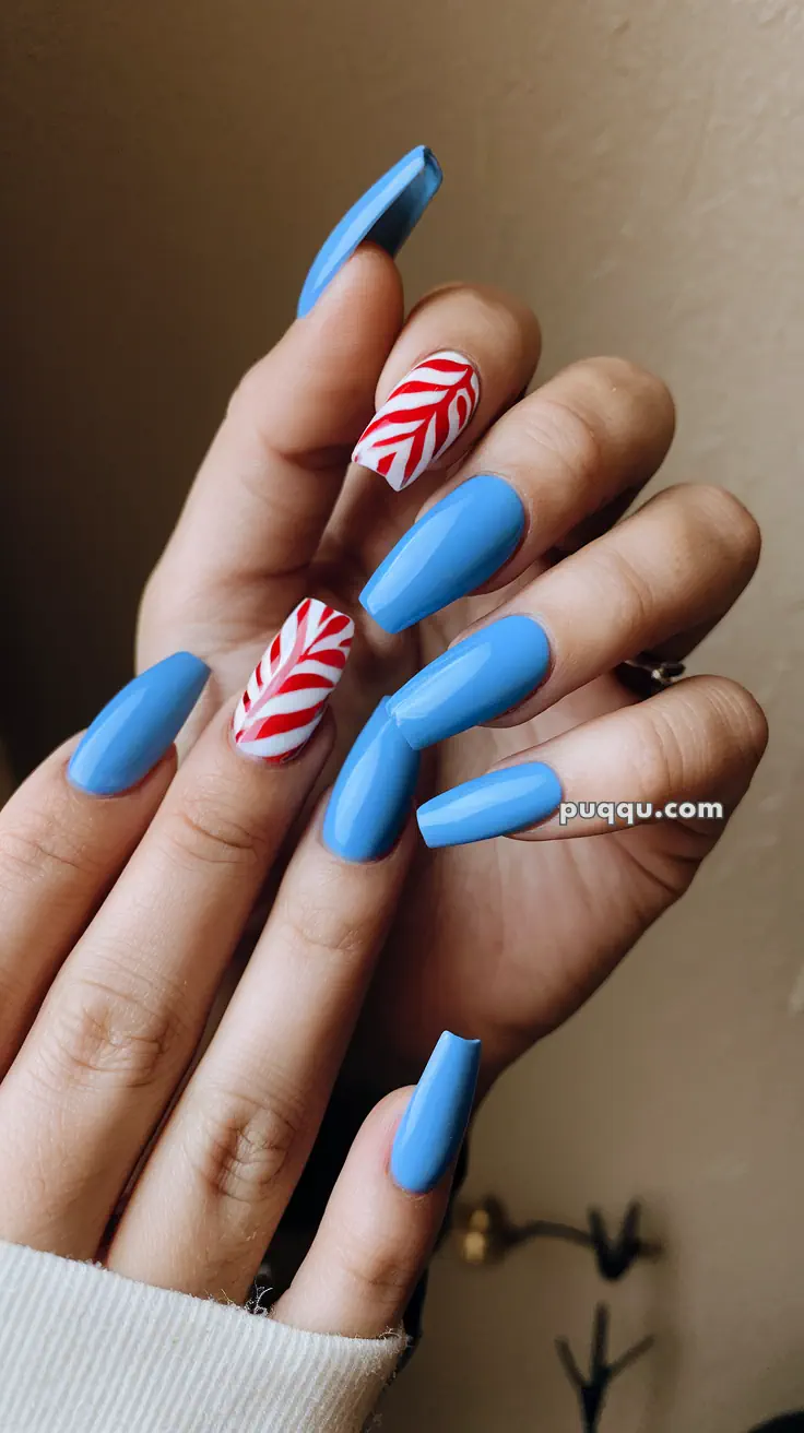 Blue and red designed acrylic nails, with one nail featuring a red and white leaf pattern.