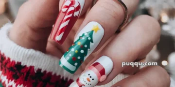 Hand with long festive nails featuring Christmas designs, including a candy cane, Christmas tree, snowman, and gift, with a green, red, and white sweater background.