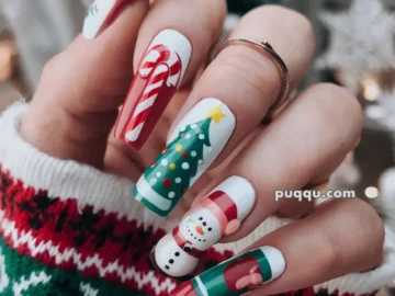 Hand with long festive nails featuring Christmas designs, including a candy cane, Christmas tree, snowman, and gift, with a green, red, and white sweater background.