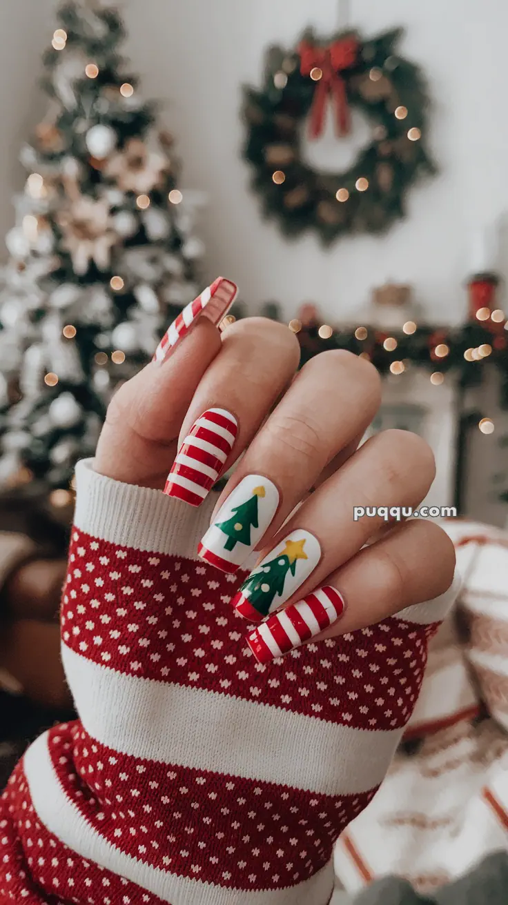 Hand with Christmas-themed nail art featuring candy cane stripes and Christmas trees, set against a festive holiday background with a wreath and tree.