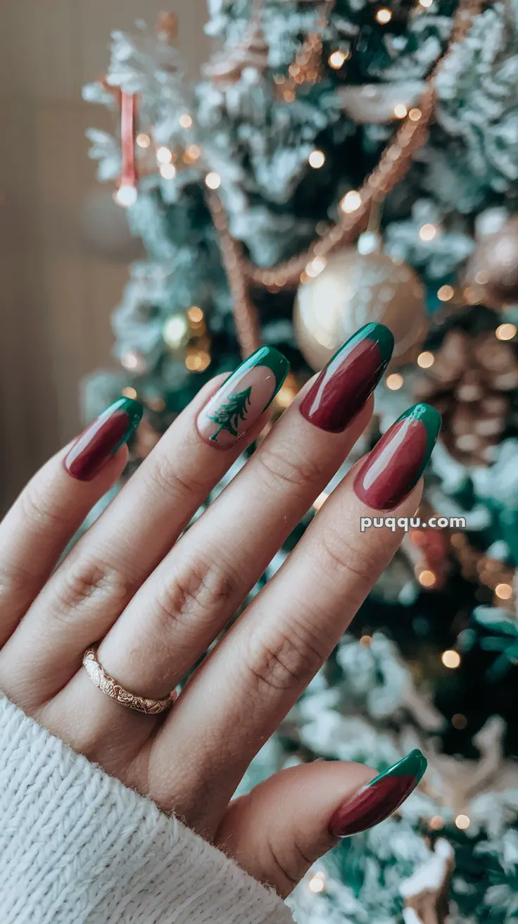 A hand with Christmas-themed nail art, featuring green and red nails with a small Christmas tree design on the ring finger, against a blurred Christmas tree background.