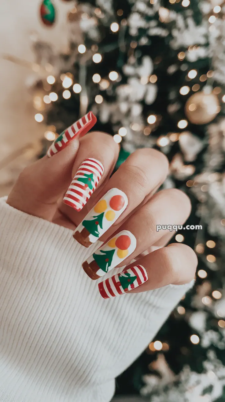 Close-up of festive nail art featuring red and white stripes with Christmas tree designs, against a blurred background of a decorated Christmas tree.