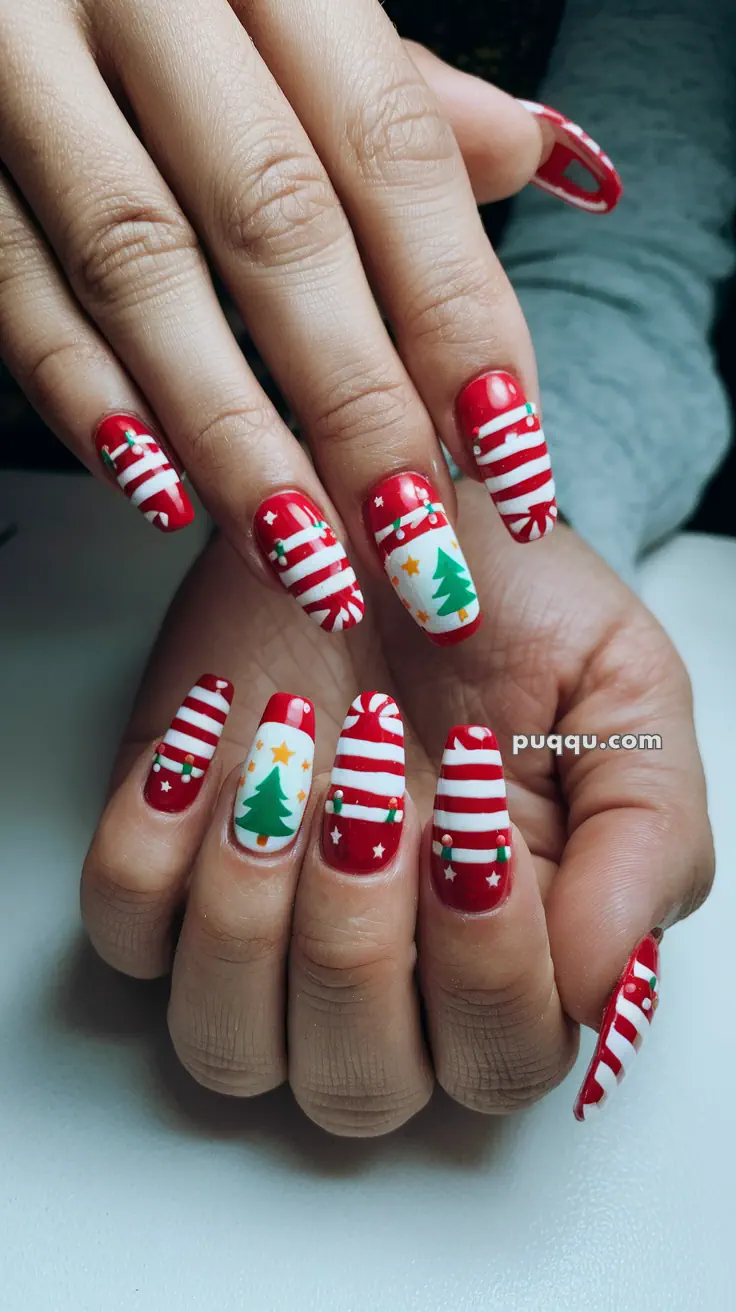 Hands with long nails painted with a festive Christmas design featuring red and white stripes, Christmas trees, stars, and small bow accents.