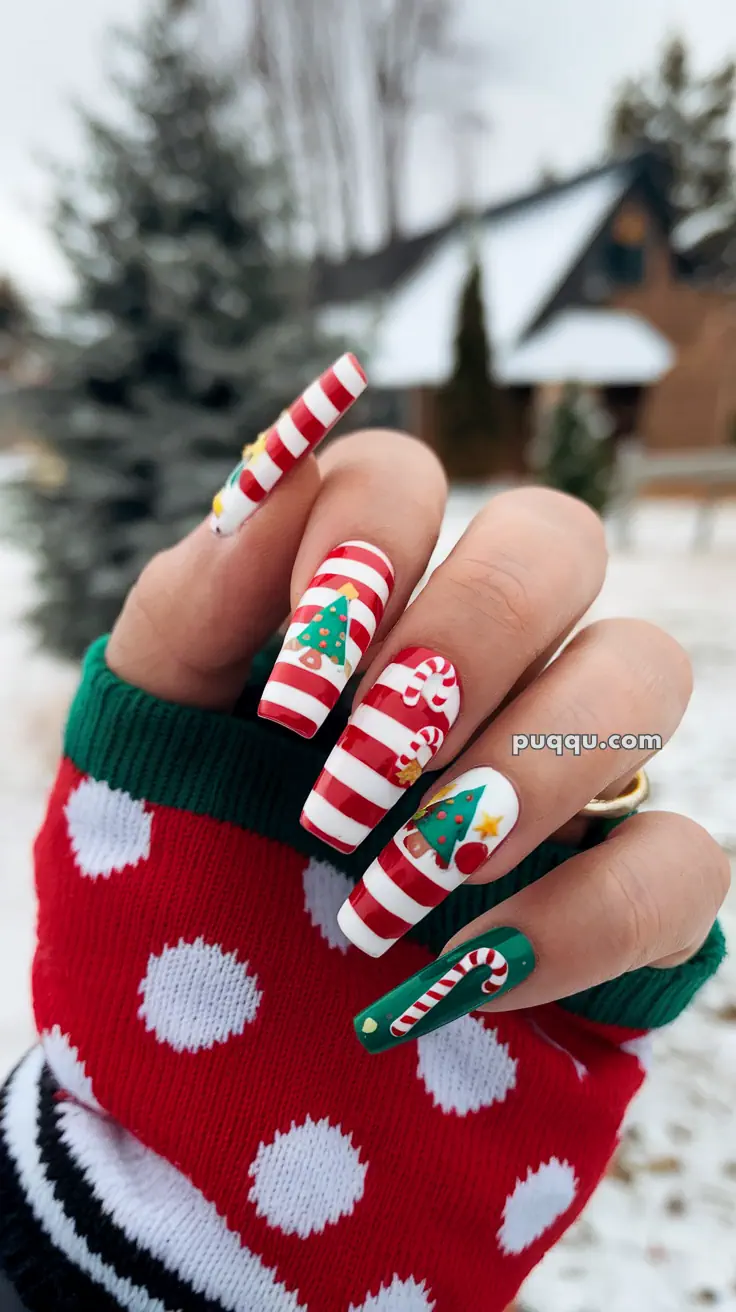 Festive Christmas-themed nail art with red and white stripes, Christmas trees, and candy canes on long nails, with a polka dot red and white sweater in the background.