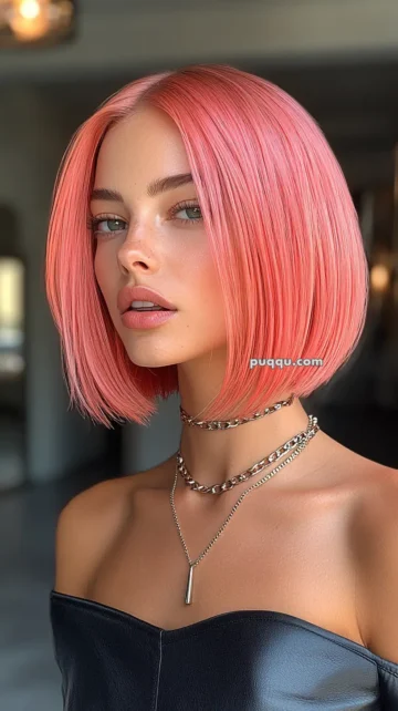 A person with short, pink hair and minimal makeup, wearing a strapless black top and layered chain necklaces.