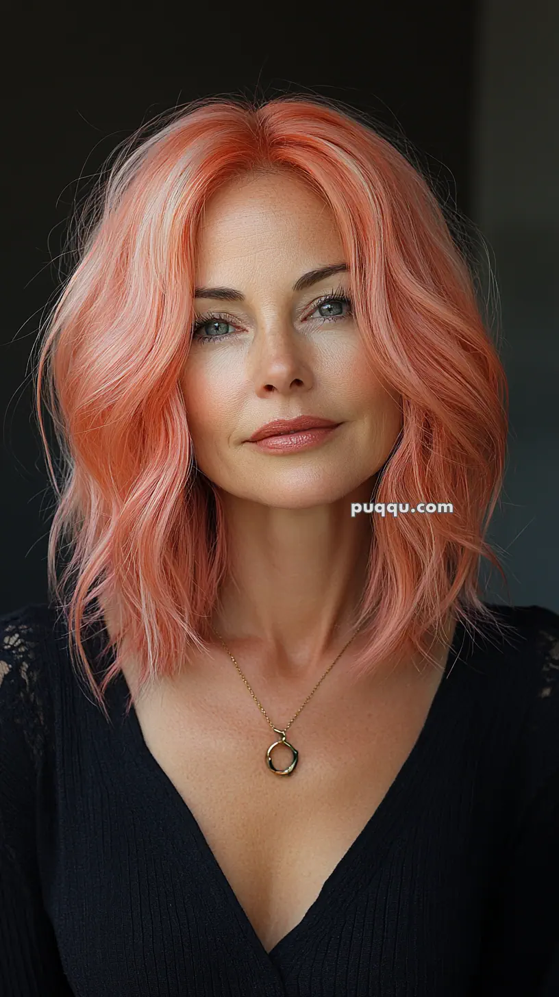 A woman with peach-colored hair and a black top, wearing a necklace with a circular pendant.