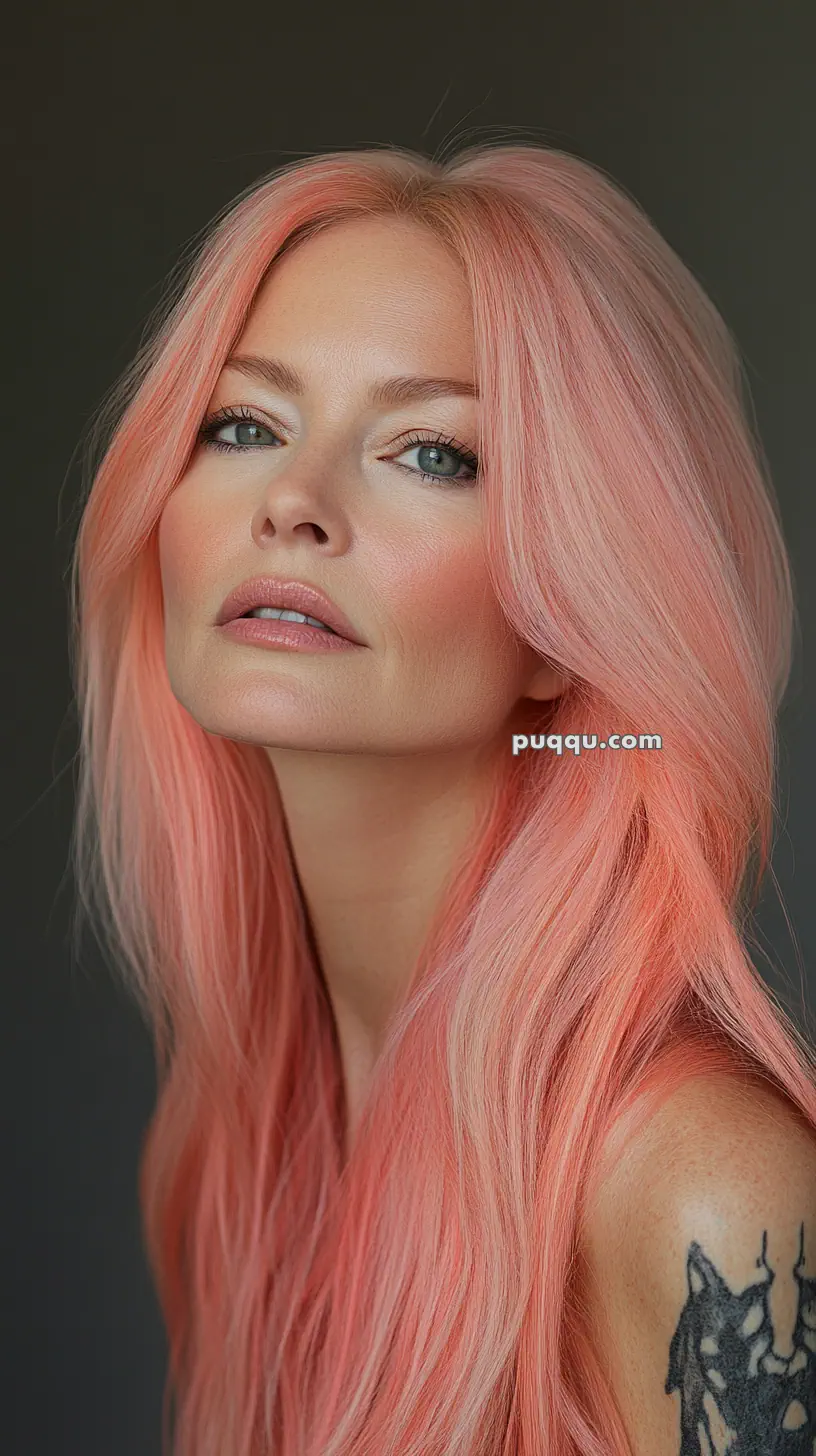 A person with long pastel pink hair, pale skin, and visible tattoo on their shoulder, looking towards the camera.